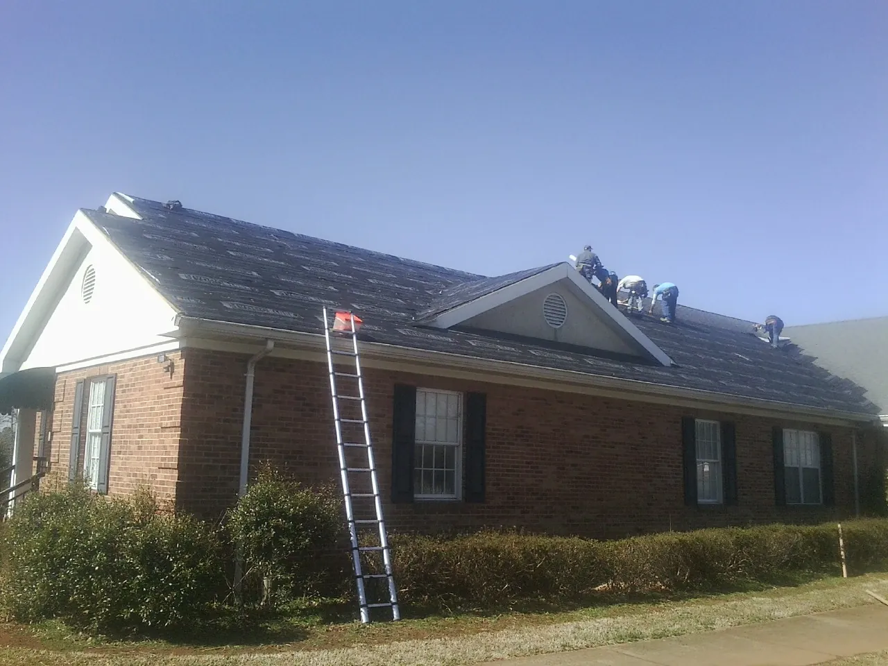 Crew tearing shingles off a brick ranch roof with a ladder set — Emergency Roof Repair work by our crew in Ben Lomond