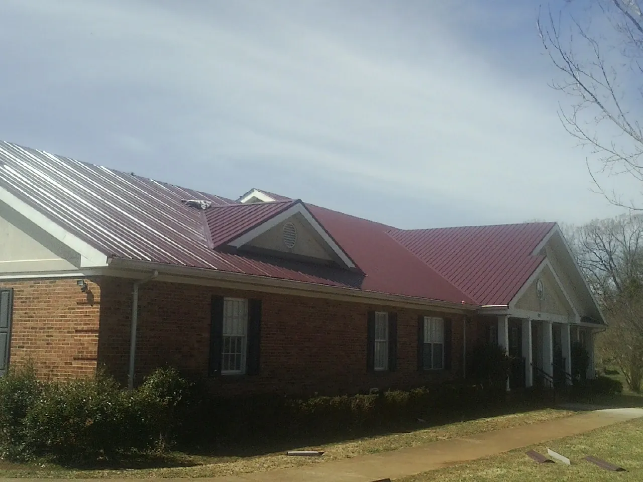 Red metal roof with gabled entries on a long brick building, from a Hail Damage Roof Repair job in Ben Lomond