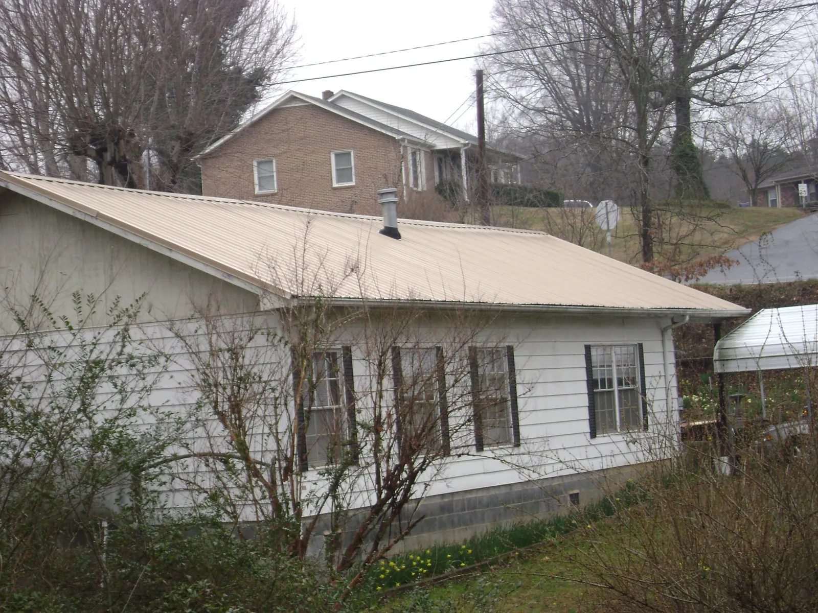Tan metal roof on a white sided house set into a hillside — Commercial Roofing by Roofing Brothers in Ben Lomond